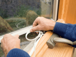 Home Inspector installing weatherstripping along a window frame to seal air leaks and improve home energy efficiency